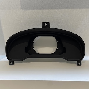May include: Black plastic gauge pod for a car dashboard. The pod has a large circular opening for a gauge and several smaller holes for mounting screws.
