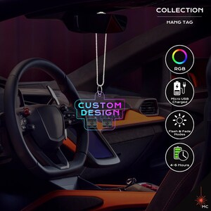 Puede incluir: Un colgante para coche con las palabras "CUSTOM DESIGN" en una fuente de neón. La etiqueta está suspendida de una cadena y cuelga frente al salpicadero de un coche. Tiene RGB, carga Micro USB, modos flash y desvanecimiento y una duración de batería de 4-6 horas.