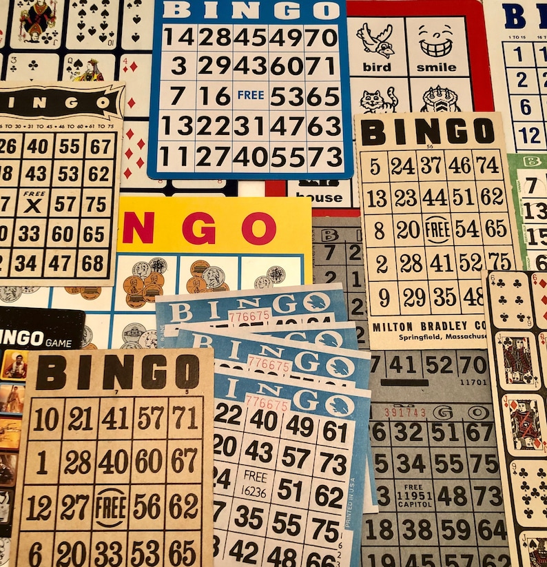 May include: A close-up of several bingo cards with numbers and the word "FREE" in the center of each card. The cards are on a table with other bingo cards and a yellow and red sign that says "Bingo".