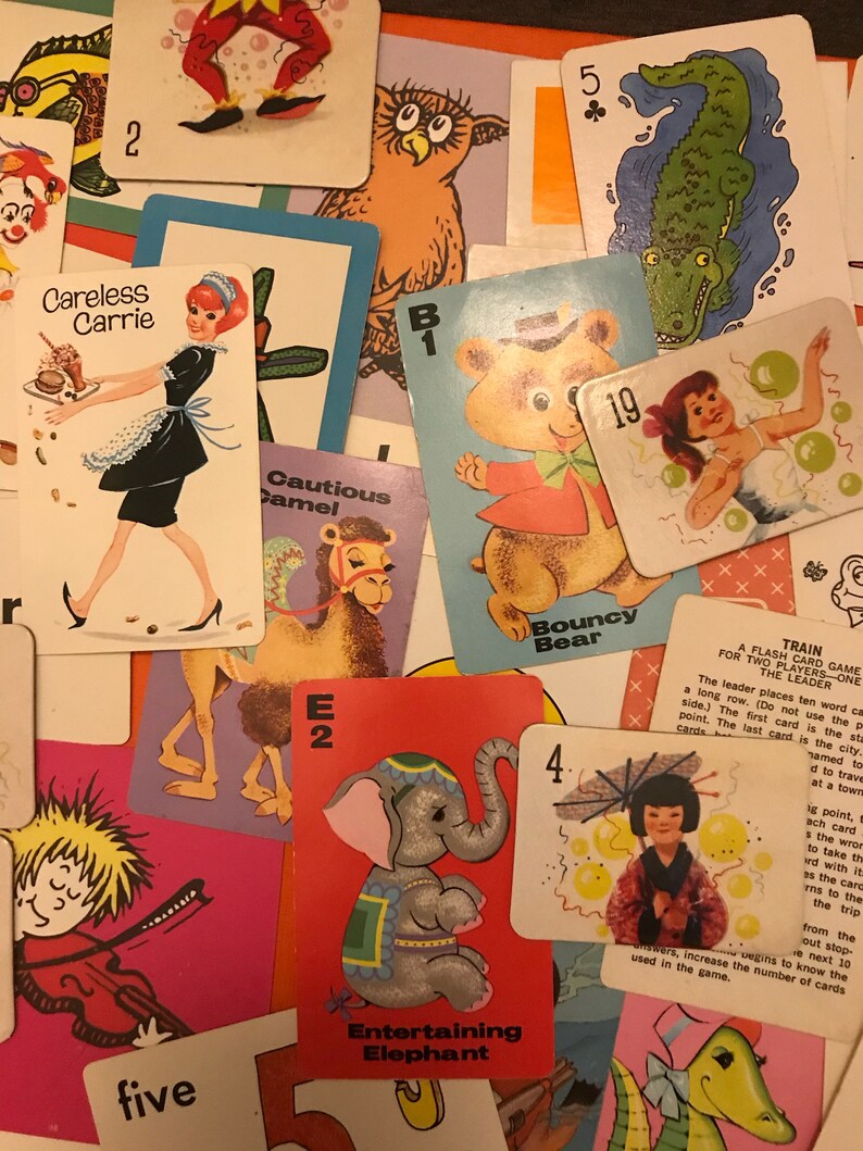 May include: A collection of colorful cards featuring various animals and characters. The cards include a camel, an elephant, a bear, a clown, an owl, a crocodile, and a girl with balloons. The cards are numbered and have a letter and a word on them. The cards are part of a game called "A Train for Two Players - One Flash Card Game".