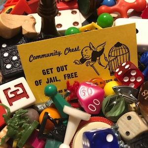 May include: A close-up of a variety of game pieces and a Community Chest card that reads "Get Out of Jail, Free". The pieces include dice, game tokens, and a Monopoly man figure.