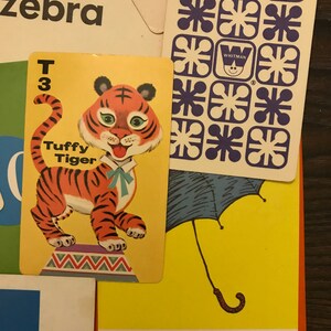 May include: A yellow card with a cartoon tiger on it. The tiger is orange and black with a blue bow tie. The card says "Tuffy Tiger" and "T 3".