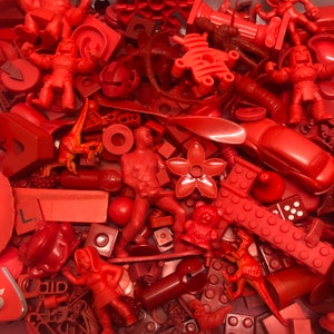 May include: A collection of red plastic toys, including dinosaurs, robots, cars, and building blocks. The toys are all in various shapes and sizes.
