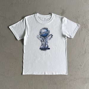 Könnte beinhalten: Weißes T-Shirt mit einer blau-weißen Grafik eines Globus, der von einer geflügelten Statue gehalten wird. Der Text "THE WORLD IS LOOKS" steht über dem Globus. Das Shirt ist aus weichem Material.