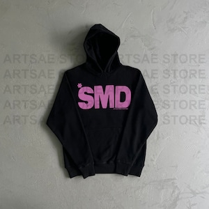 May include: Black hooded sweatshirt with a pink "SMD" logo printed on the front. The logo has a small asterisk above the "S".