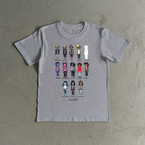 以下が含まれることがあります： 様々な衣装やアクセサリーを身につけた、ユニークなキャラクターのピクセル化されたグラフィックが特徴のグレーのTシャツです。「Lucki」の文字がキャラクターの下にプリントされています。さまざまな色とスタイルが使用されており、視覚的に魅力的で芸術的なデザインです。