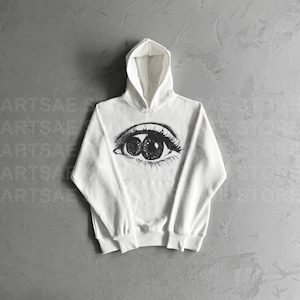 May include: White hooded sweatshirt with a black and white graphic of an eye on the front.