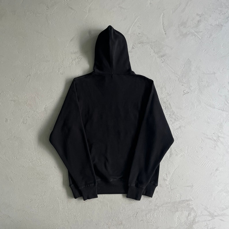 May include: A black hooded sweatshirt with a drawstring hood. The sweatshirt has long sleeves and a kangaroo pocket.
