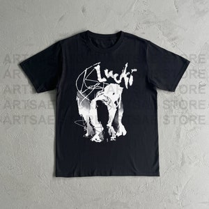 以下が含まれることがあります： 白いグラフィックプリントが施された黒いTシャツ。人物と「Lucid」という単語がスタイリッシュなフォントで書かれています。