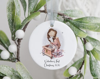 May include: A white ceramic Christmas ornament with a watercolor illustration of a ballerina, a music box, and a rocking horse. The ornament has a light blue ribbon for hanging and the text "Valentina's First Christmas 2020".