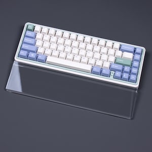 May include: A white and light blue mechanical keyboard with a clear acrylic wrist rest. The keyboard has a light blue and white color scheme with a green accent key.