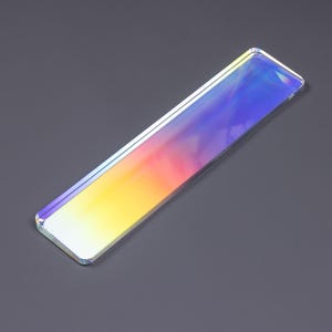 May include: A rectangular, clear acrylic bar featuring a vibrant, iridescent gradient finish that shifts from warm yellow and orange tones at one end to cool blue and purple hues at the other, with smooth, rounded corners and a polished, reflective surface.