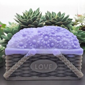 May include: A purple soap bar shaped like a basket overflowing with flowers. The basket has a woven texture and the word "LOVE" is embossed on the front.