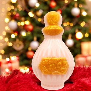 May include: A white and gold decorative bottle with a gold label that says "Spice" in a decorative font. The bottle is sitting on a red fuzzy surface.