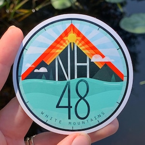 May include: A round sticker with a blue, green, and orange design. It features a mountain range with a sun rising behind it. The text "NH 48 WHITE MOUNTAINS" is printed around the edge.