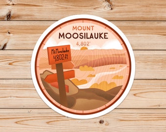 Op de afbeelding: Een ronde sticker met een bruine, oranje en witte illustratie van een berglandschap. De sticker heeft de tekst "MOUNT MOOSILAUIKE 4,802'" en een bord met de tekst "Mt. Moosil auke 4,802 ft."