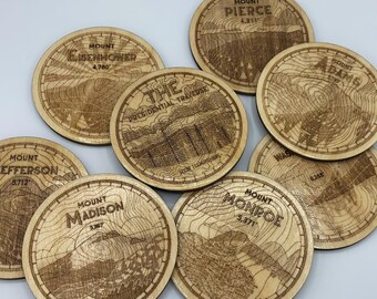 May include: A set of nine wooden coasters featuring engraved maps of mountains in the Presidential Traverse, including Mount Eisenhower, Mount Jefferson, Mount Madison, Mount Monroe, Mount Pierce, and Mount Adams. Each coaster features the name of the mountain and its elevation in feet.