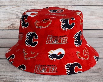 Puede incluir: Sombrero de pescador rojo con un patrón de logotipo de Calgary Flames en blanco y negro. El sombrero tiene un ala ancha y una corona plana.