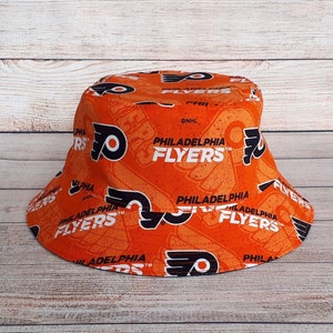 May include: Orange bucket hat with a black and white print of the Philadelphia Flyers logo and the words "Philadelphia Flyers".