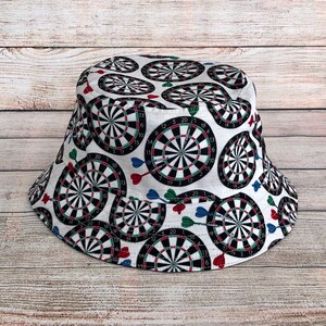 May include: A white bucket hat with a pattern of black and white dartboards and red, green, and blue darts.