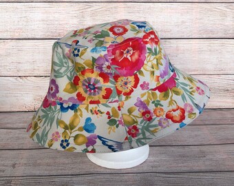 May include: A white bucket hat with a floral print featuring red, pink, yellow, blue, and green flowers. The hat has a wide brim and a flat crown.