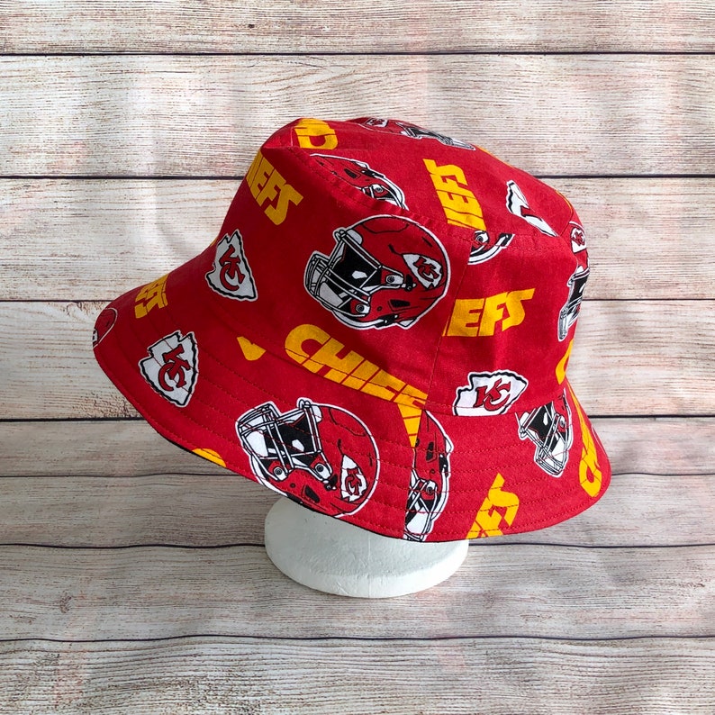 May include: Red bucket hat with a yellow and white pattern of the Kansas City Chiefs logo and the word "Chiefs".