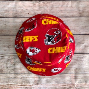 May include: Red and yellow bucket hat with a Kansas City Chiefs pattern. The hat features the team logo, the words "Chiefs" and a football helmet.