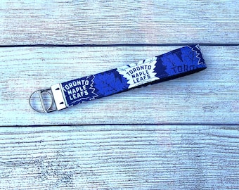 Pode incluir: Um chaveiro de tecido azul e branco com o texto "Toronto Maple Leafs" e um design de folha de bordo.