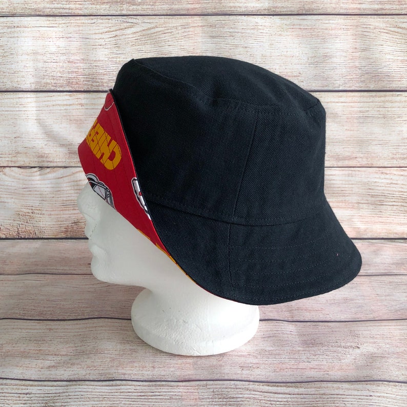 May include: Black bucket hat with a red, yellow, and white patterned lining. The lining features the word "CHEER" and a cartoon character.