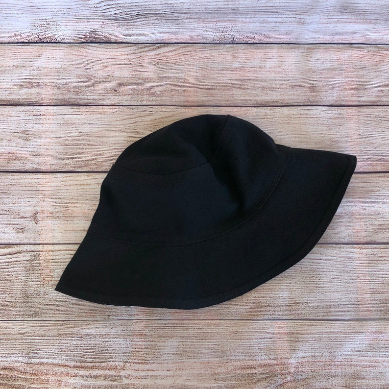 May include: A black bucket hat made of a soft fabric. The hat has a wide brim and a simple design.