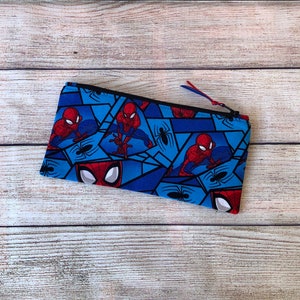 Puede incluir: Un estuche para l&aacute;pices con cremallera azul y rojo con un patr&oacute;n repetido de personajes de Spiderman.