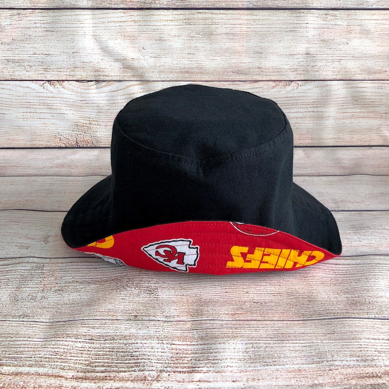 May include: Black bucket hat with a red and yellow Kansas City Chiefs logo print on the brim.