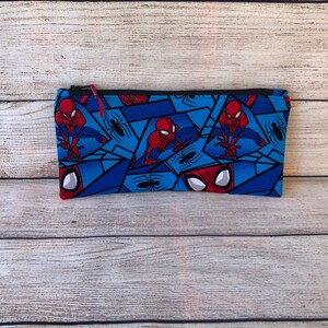 Puede incluir: Un estuche para l&aacute;pices azul con cremallera con un patr&oacute;n repetido de Spiderman con un traje rojo y azul, con un dise&ntilde;o de telara&ntilde;a negra.