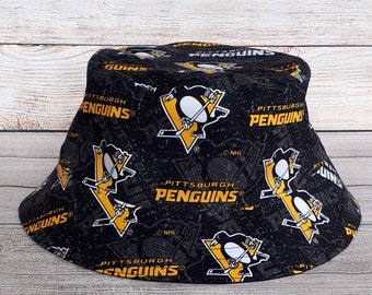 May include: Black bucket hat with a repeated pattern of the Pittsburgh Penguins logo. The logo is yellow and black with a penguin holding a hockey stick. The text "Pittsburgh Penguins" is written in yellow on the logo.