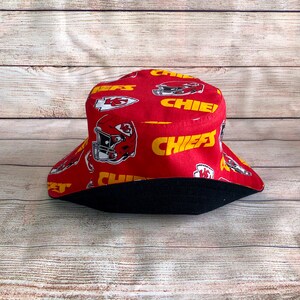 May include: Red bucket hat with a black brim and a pattern of yellow "Chiefs" text and red and white football helmets.