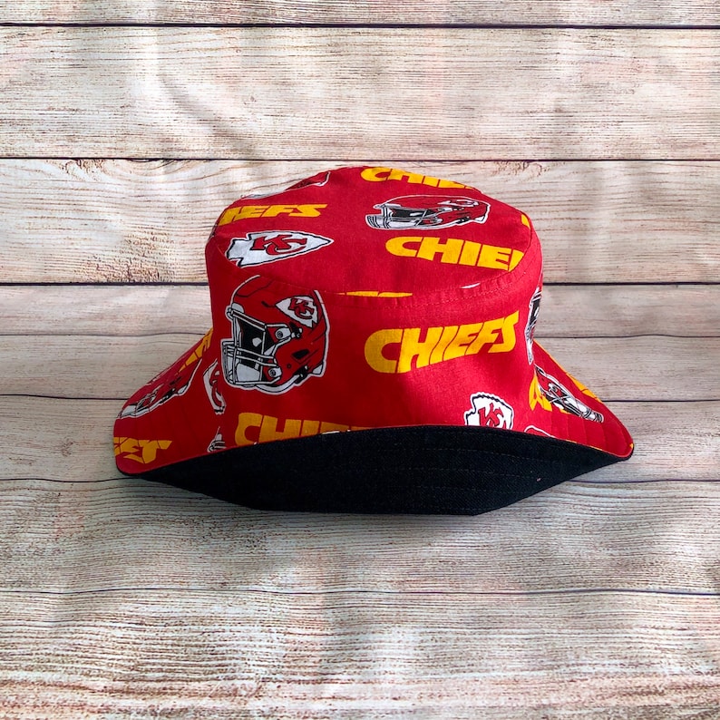 May include: Red bucket hat with a black brim and a pattern of yellow "Chiefs" text and red and white football helmets.