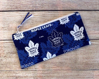 May include: A rectangular, zippered pouch with a blue and white maple leaf pattern. The text "TORONTO MAPLE LEAFS" is printed on the pouch. The zipper pull is white and blue.