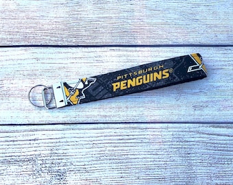 Könnte beinhalten: Schwarzer und gelber Schlüsselanhänger mit einem Pittsburgh Penguins Logo und dem Text "Pittsburgh Penguins" auf schwarzem Hintergrund.