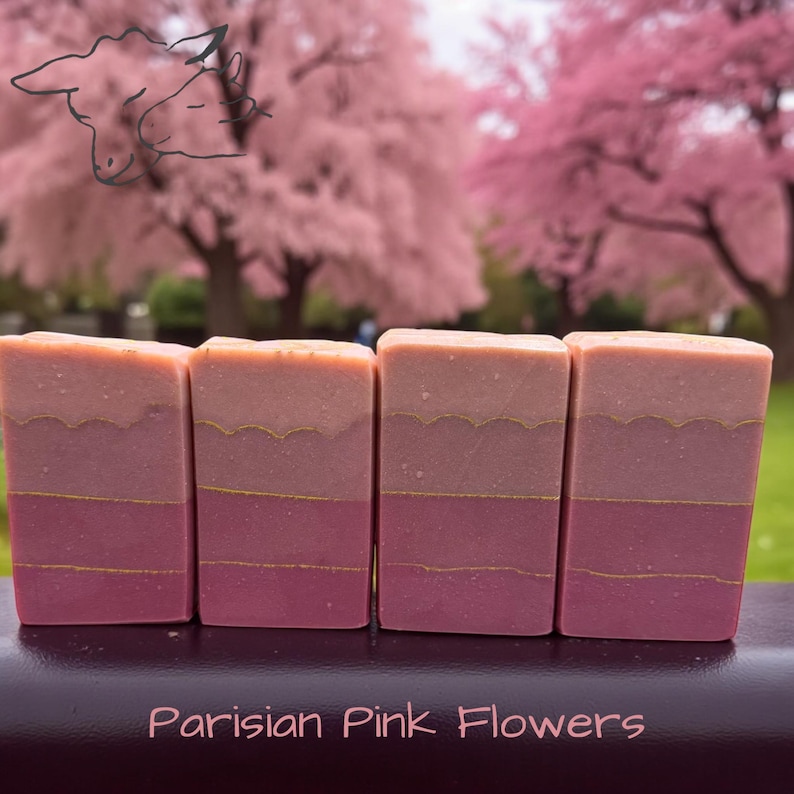 Puede incluir: Cuatro barras de jab&oacute;n rectangulares dispuestas en fila, cada una con capas horizontales en tonos rosa y melocot&oacute;n separadas por finas l&iacute;neas doradas. El texto "Parisian Pink Flowers" est&aacute; impreso en rosa claro en la parte inferior.