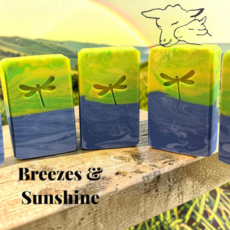 Puede incluir: Pastillas de jab&oacute;n rectangulares con un degradado de amarillo, verde y azul con un dise&ntilde;o de lib&eacute;lula en relieve. El texto Breezes & Sunshine est&aacute; impreso debajo de las pastillas. Un dibujo lineal de dos cabezas de oveja es visible arriba a la derecha.