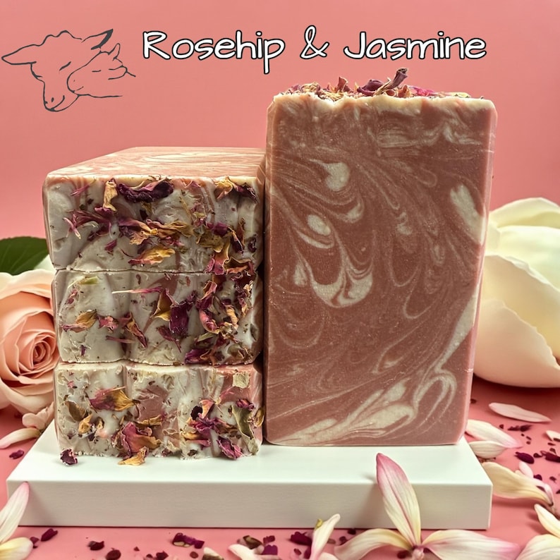 May include: A stack of three rectangular soaps and a single soap bar. The soaps are decorated with dried flower petals. The single bar has a pink and white swirl pattern. The text "Rosehip & Jasmine" is at the top.