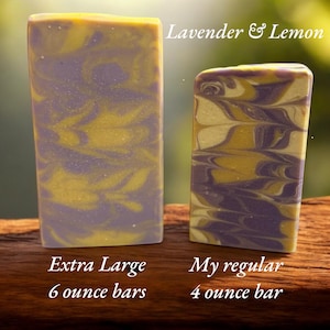 May include: Two rectangular bars of Lavender & Lemon soap with a marbled purple and yellow pattern. The larger bar is labeled as an Extra Large 6 ounce bar, while the smaller bar is labeled as My regular 4 ounce bar, indicating their respective sizes.