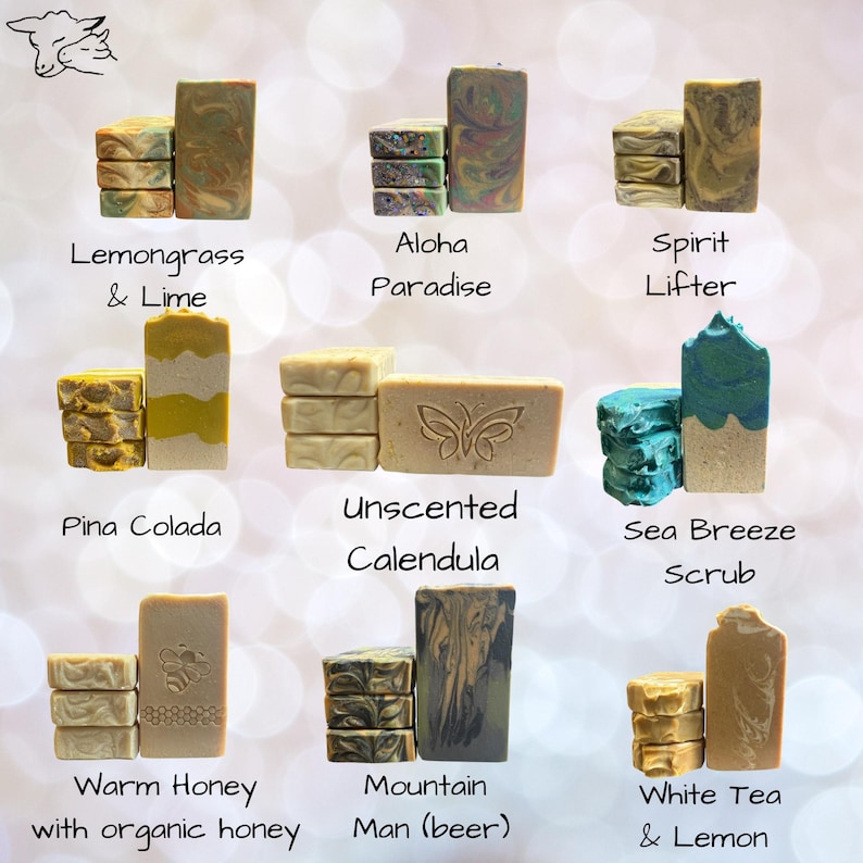 May include: A collection of nine varieties of rectangular soap bars, each labeled with names including Lemongrass & Lime, Aloha Paradise, Spirit Lifter, Pina Colada, Unscented Calendula, Sea Breeze Scrub, Warm Honey, Mountain Man, and White Tea & Lemon.
