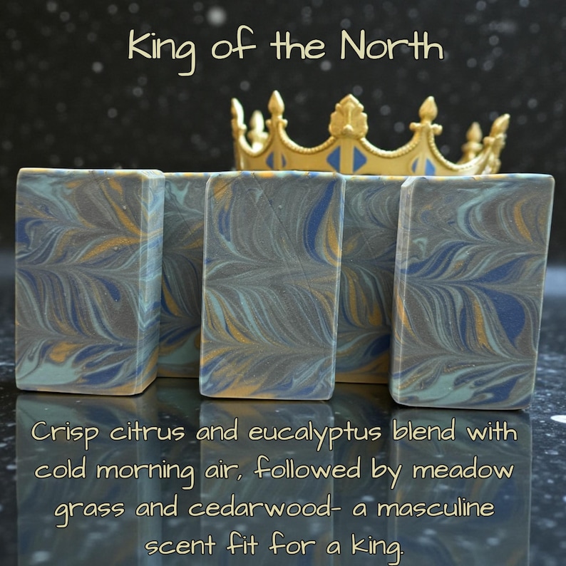 May include: Artisan soap bars with a marbled design in shades of gray, blue, and gold, with the text "King of the North." A gold crown sits behind the soaps. The text describes the scent as crisp citrus and eucalyptus.