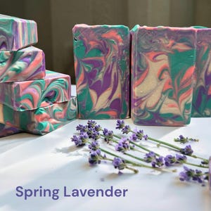 May include: Handmade soap bars with a colorful swirl design in shades of teal, purple, pink, and cream. The bars are stacked and arranged with sprigs of lavender. The text "Spring Lavender" is at the bottom.
