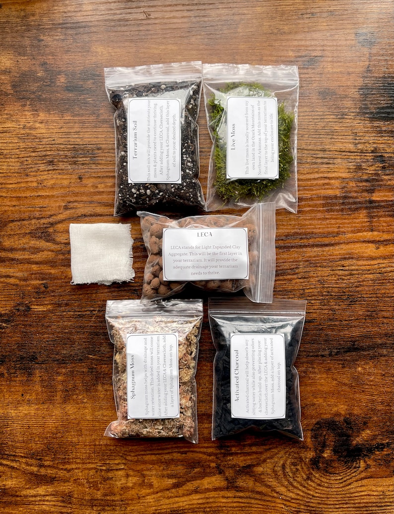 May include: A terrarium kit with soil, moss, charcoal, and other components in clear plastic bags. The kit includes Terrarium Soil, Live Moss, LECA, Sphagnum Moss, Activated Charcoal, and a cheesecloth. The items are arranged on a wooden surface.