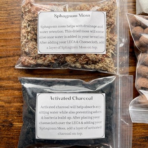 May include: Two clear plastic bags containing terrarium supplies. One bag holds dried Sphagnum Moss, with text describing its use for drainage and water retention. The other bag contains Activated Charcoal, with text explaining its function in absorbing water and preventing odors.