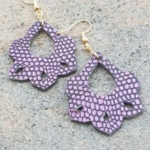 May include: A pair of purple leather earrings with a floral design and gold hooks.