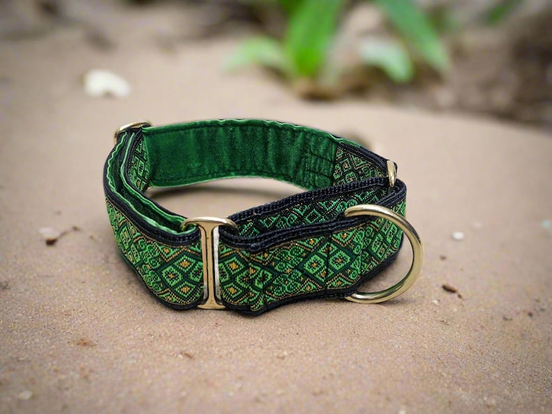 May include: A green and black fabric collar featuring a repeating geometric diamond pattern. The collar includes gold-toned metal hardware, specifically a rectangular slide and a D-ring, and is lined with a solid green fabric on the interior.