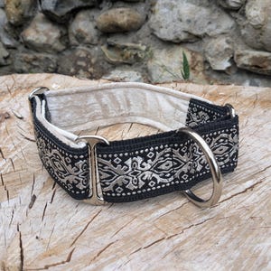 May include: A dog collar featuring a black fabric strap with a silver-toned geometric pattern, a cream-colored velvet lining, and silver-toned metal hardware including a D-ring and a sliding adjustment buckle for a secure fit around the neck.